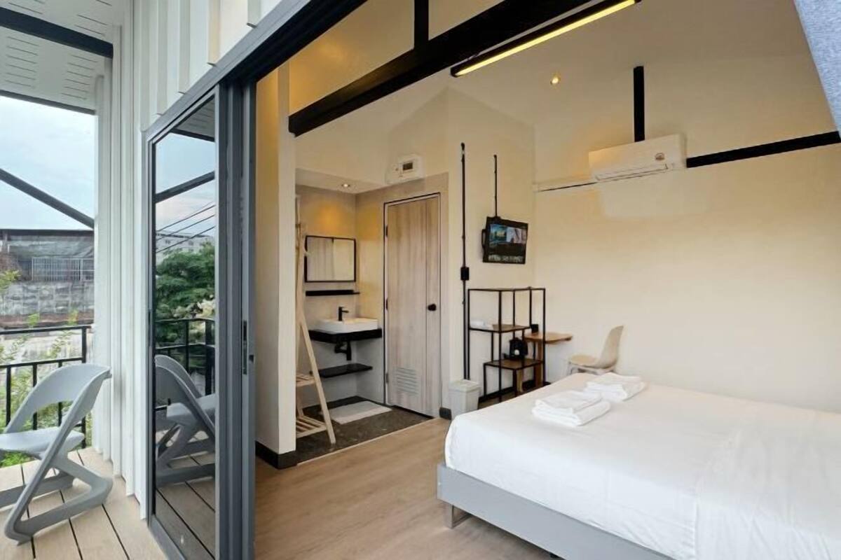 Een moderne hotelkamer met een bed, een badkamer met een wastafel en spiegel, een televisie en een balkon met stoelen.