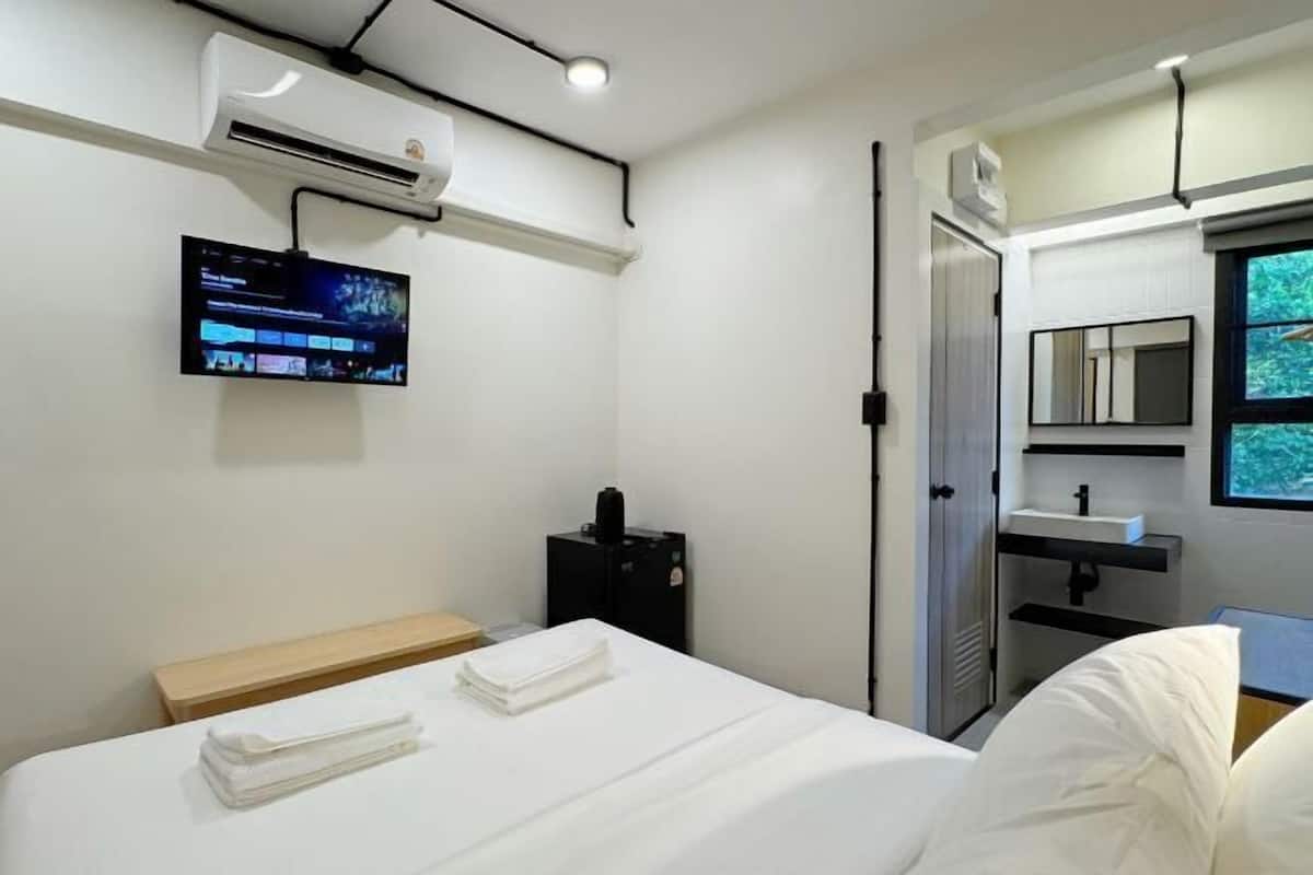 Hotelkamer met een bed, een aan de muur bevestigde televisie, een klein zwart kastje, een spiegel en een raam met uitzicht.