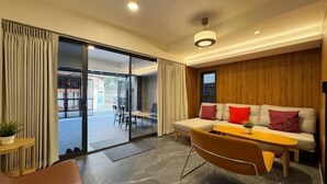 Een moderne woonkamer met een bank, een eettafel en een stoel. Er is een schuifdeur die leidt naar een buitenruimte.