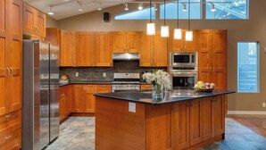 A modern kitchen with wooden cabinets, stainless steel appliances, and a large island. - Sleeps 18! Game Room, Deck w/ Firepit, 5BDR, Casita | Cedar & Stone by AvantStay (Austin)