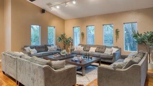 A spacious living room with a large sectional sofa, a coffee table, and multiple windows providing natural light. - Sleeps 18! Game Room, Deck w/ Firepit, 5BDR, Casita | Cedar & Stone by AvantStay (Austin)