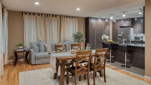A modern kitchen with dark cabinetry, a central island with bar stools, and a dining area with a wooden table and chairs. - Sleeps 18! Game Room, Deck w/ Firepit, 5BDR, Casita | Cedar & Stone by AvantStay (Austin)