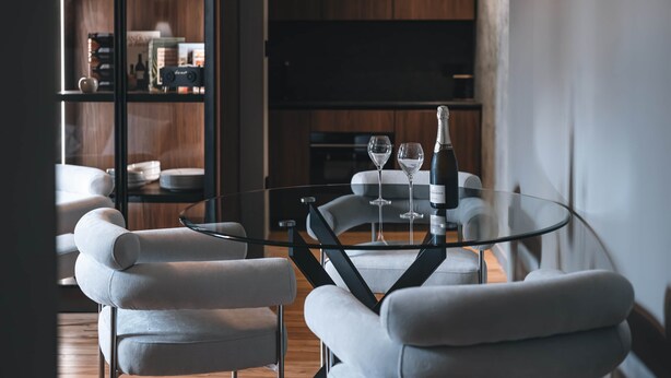 A modern dining area with a glass table surrounded by white cushioned chairs. A wine bottle and glasses are placed on the table. - Exceptional Victoire apartment (Épinal)