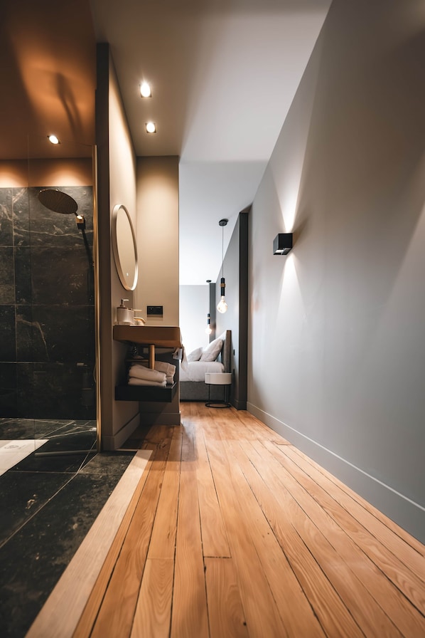 A modern bathroom with a wooden floor, a marble shower, a sink with a mirror, and a towel rack.