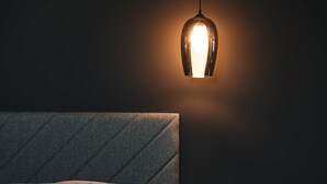 Een net opgemaakt bed met hoofdbord, nachtkastje en hanglamp.