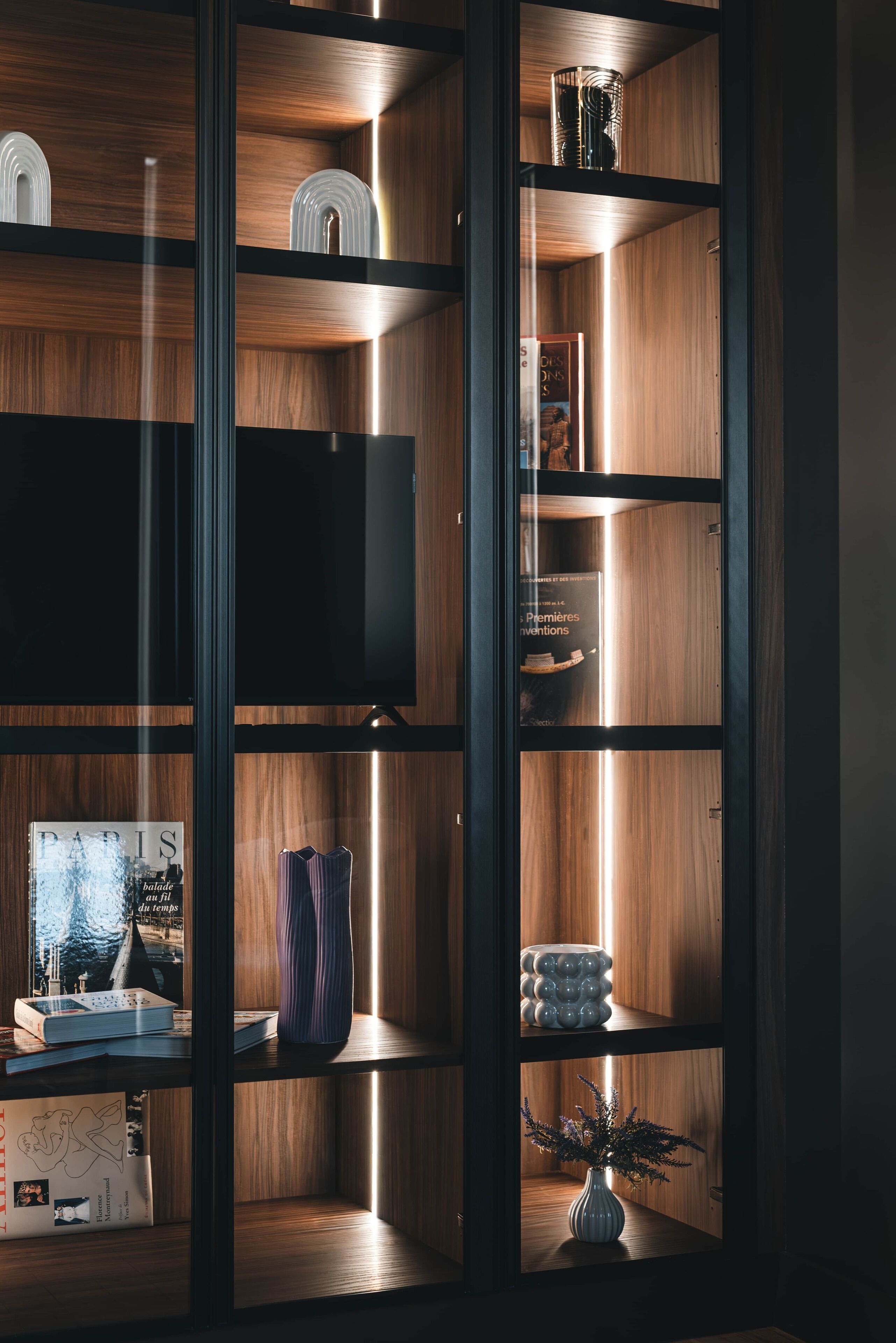 Um interior moderno com estantes de madeira, televisão de tela plana e objetos decorativos.