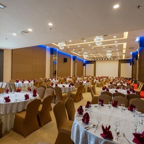 A banquet hall with round tables, chairs, and chandeliers.
