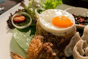 Um prato de arroz frito coberto com ovo frito, acompanhado de frango frito e legumes.