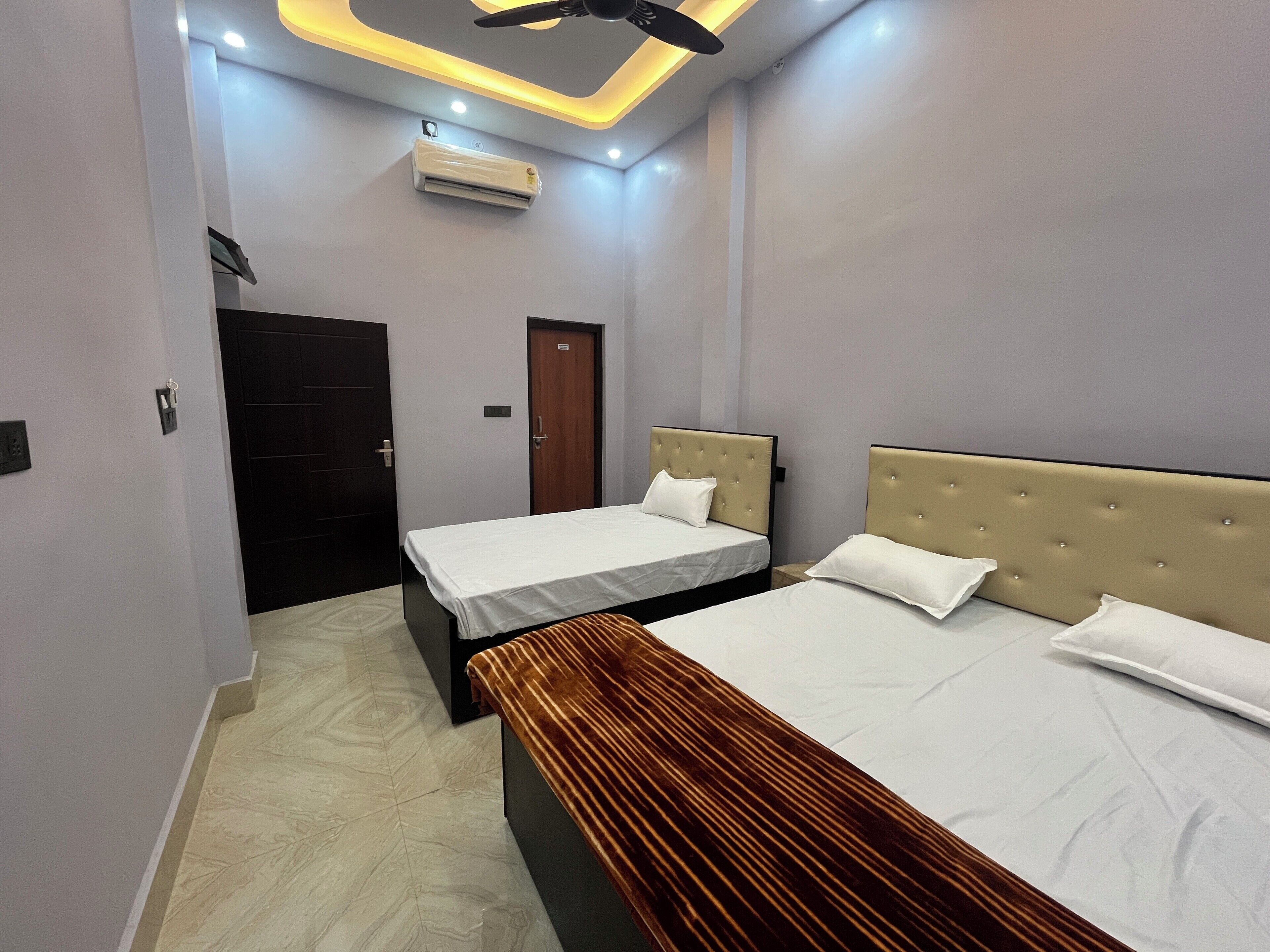 A hotel room with two beds, a ceiling fan, an air conditioner, and a door.