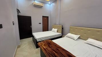 A hotel room with two beds, a ceiling fan, an air conditioner, and a door.