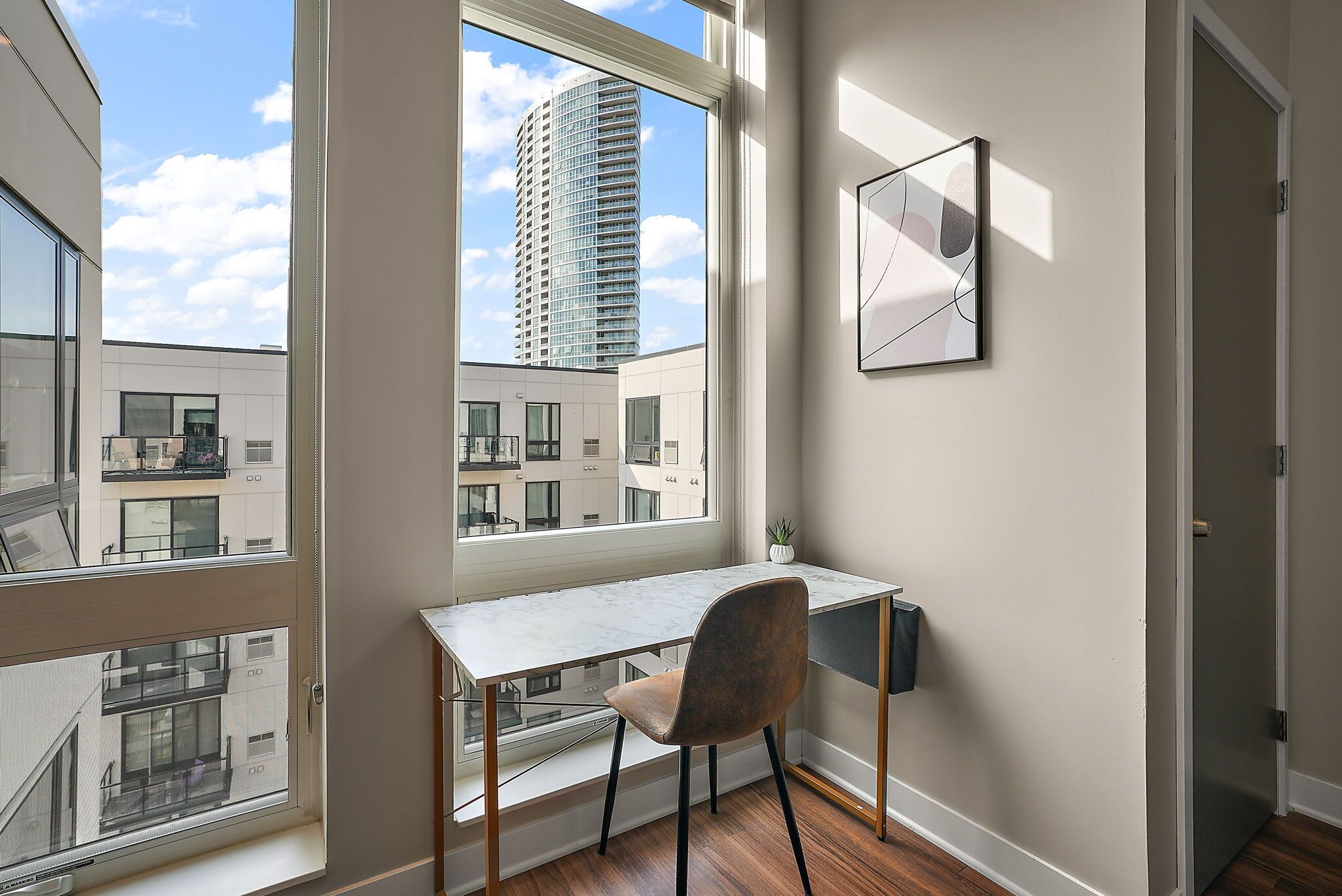 A modern apartment with a large window, a marble desk, a chair, and a framed picture on the wall.