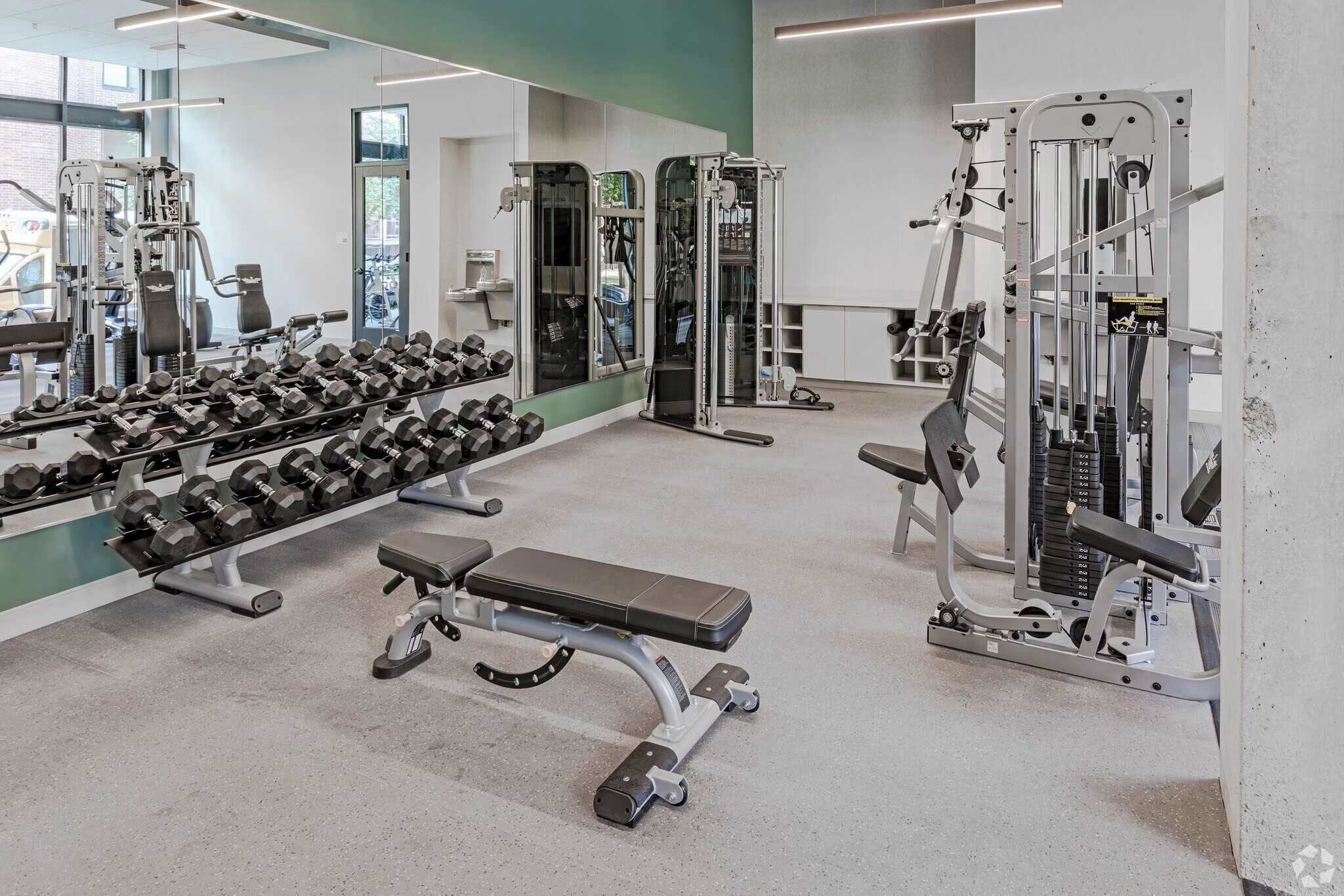 Un gimnasio con diverso equipo de ejercicio, incluyendo mancuernas, bancos y máquinas de pesas.