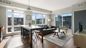 A modern apartment with a kitchen, dining area, and living room. It features large windows, a sofa, a coffee table, and a TV. - CozySuites Marquee (Minneapolis)