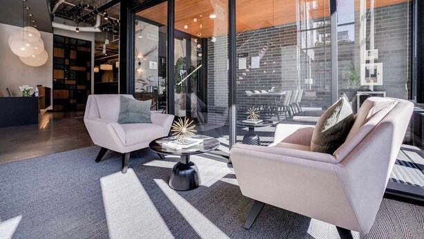 A modern interior with two sofas, a coffee table, and a glass wall offering a view of a brick building. - CozySuites Marquee (Minneapolis)