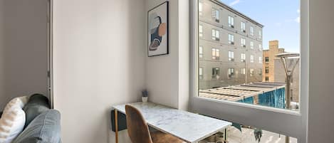 A small, modern room with a white marble table, a brown chair, and a large window overlooking a cityscape.
