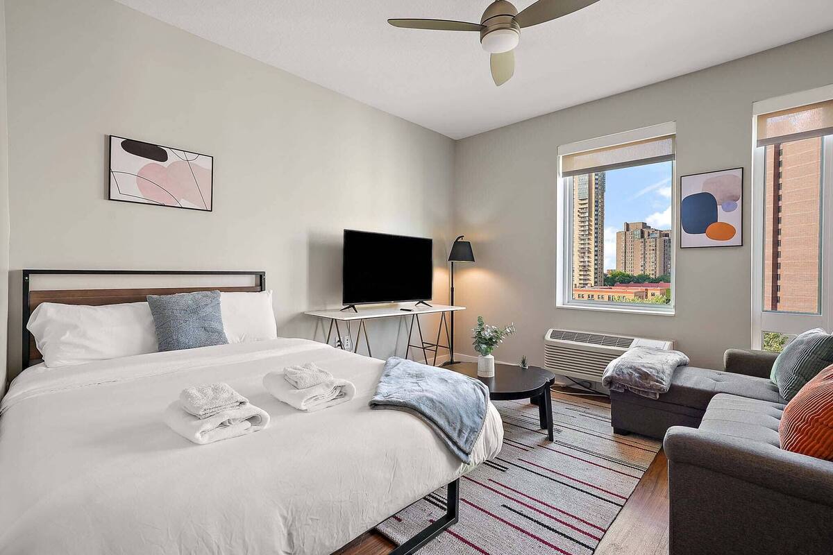 Una habitación de hotel moderna con una cama, un escritorio, un televisor y un sofá.