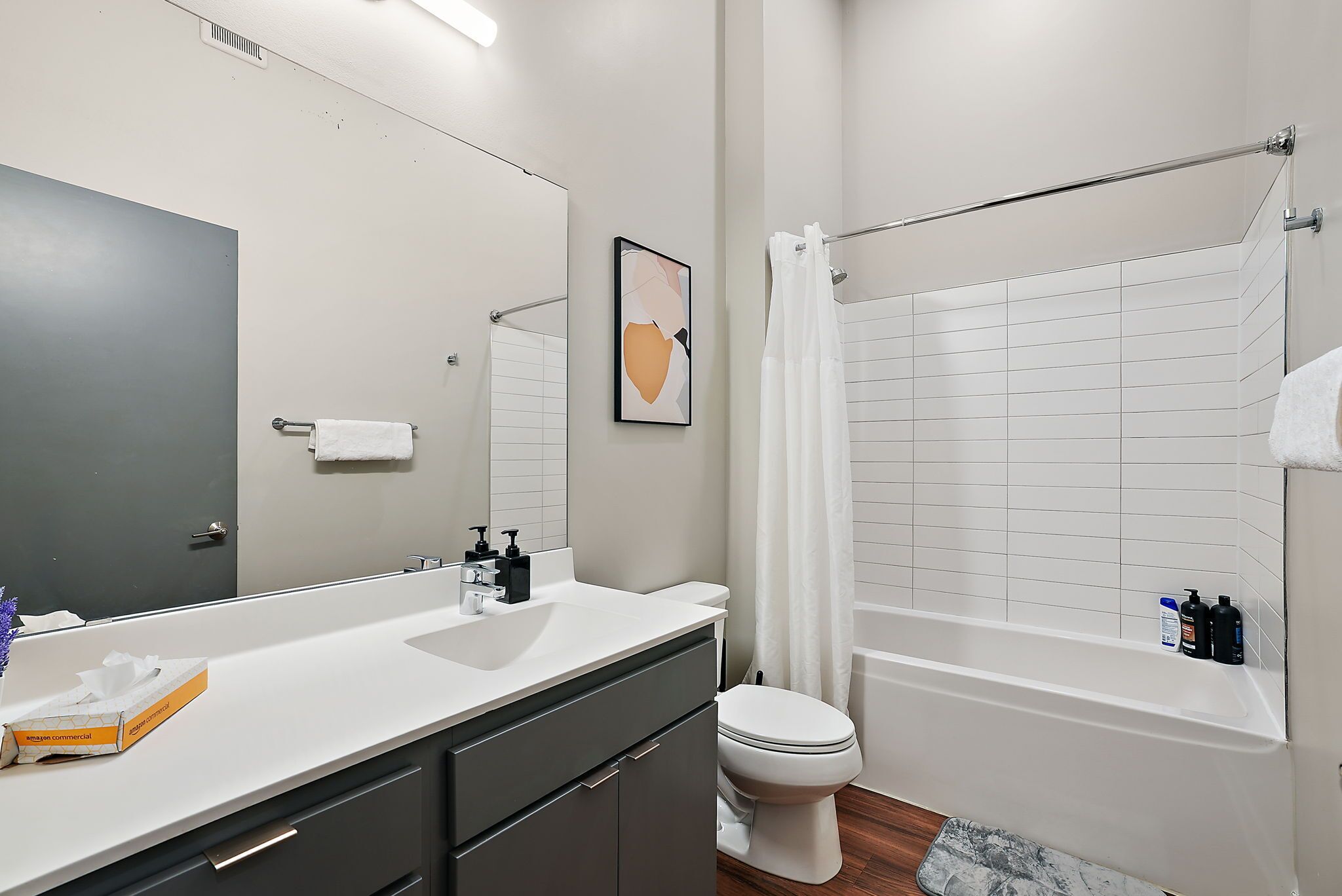 A modern bathroom with a white sink, toilet, and bathtub. There is a towel rack above the bathtub and a framed picture on the wall.