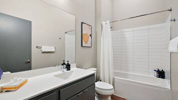 A modern bathroom with a white sink, toilet, and bathtub. There is a towel rack above the bathtub and a framed picture on the wall.