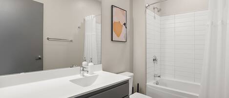 Un baño moderno con un espejo grande, lavamanos blanco y bañera.