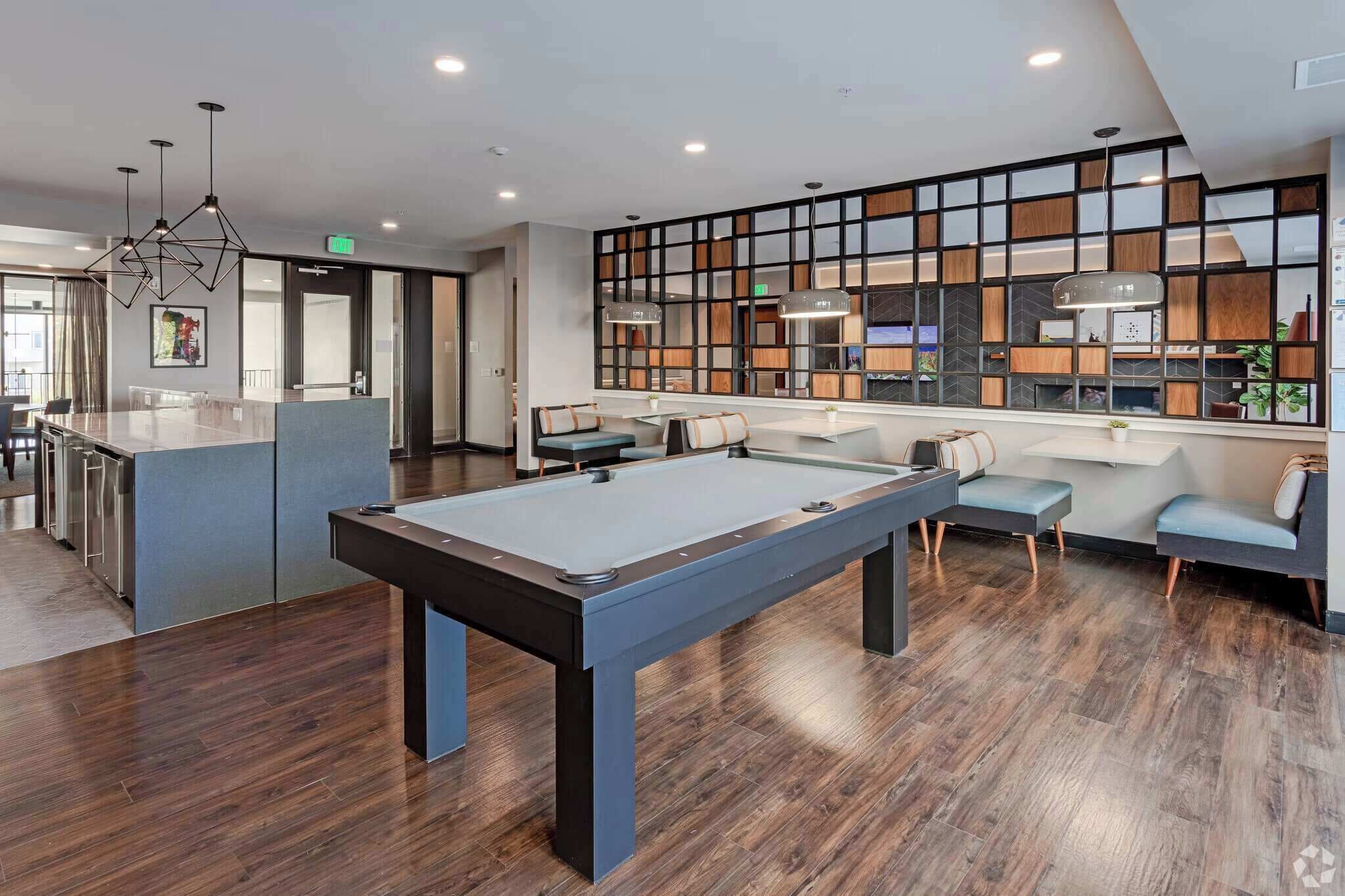 Une table de billard moderne dans une pièce bien éclairée, dotée d’un plancher en bois, de coins salon et d’une grande fenêtre offrant une vue dégagée.