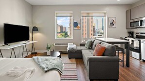 A modern living room with a flat-screen TV, sofa, and dining area. - CozySuites Marquee (Minneapolis)
