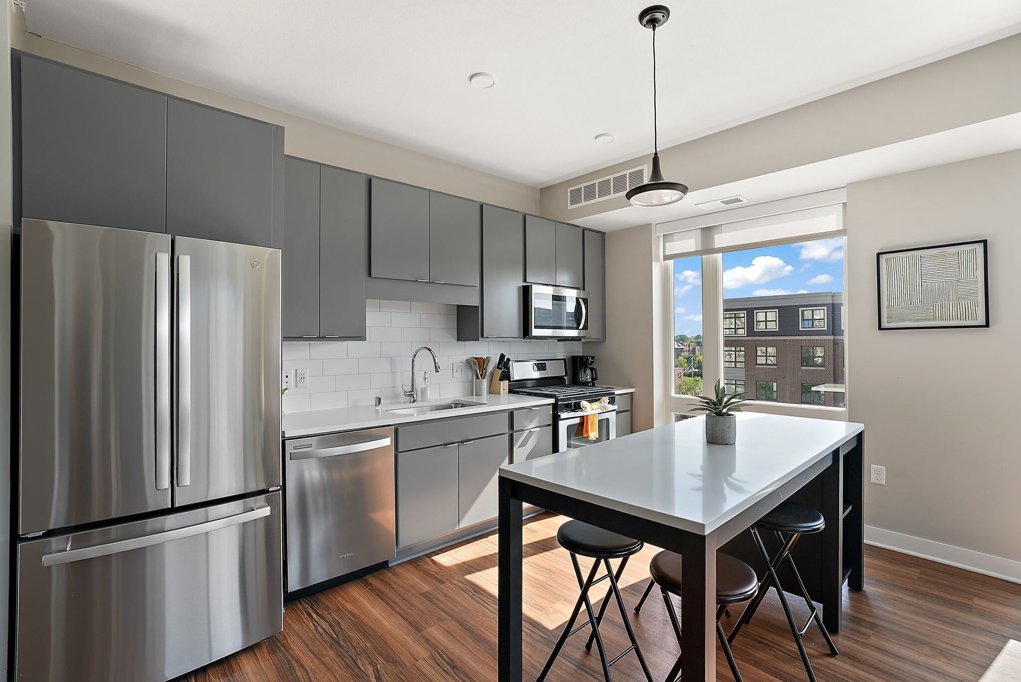 A modern kitchen with stainless steel appliances, a central island with stools, and a view of the city through large windows.