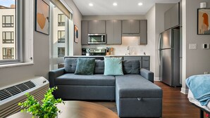 A modern living room with a sectional sofa, a dining table, and a kitchen area with grey cabinets and stainless steel appliances. - CozySuites Marquee (Minneapolis)