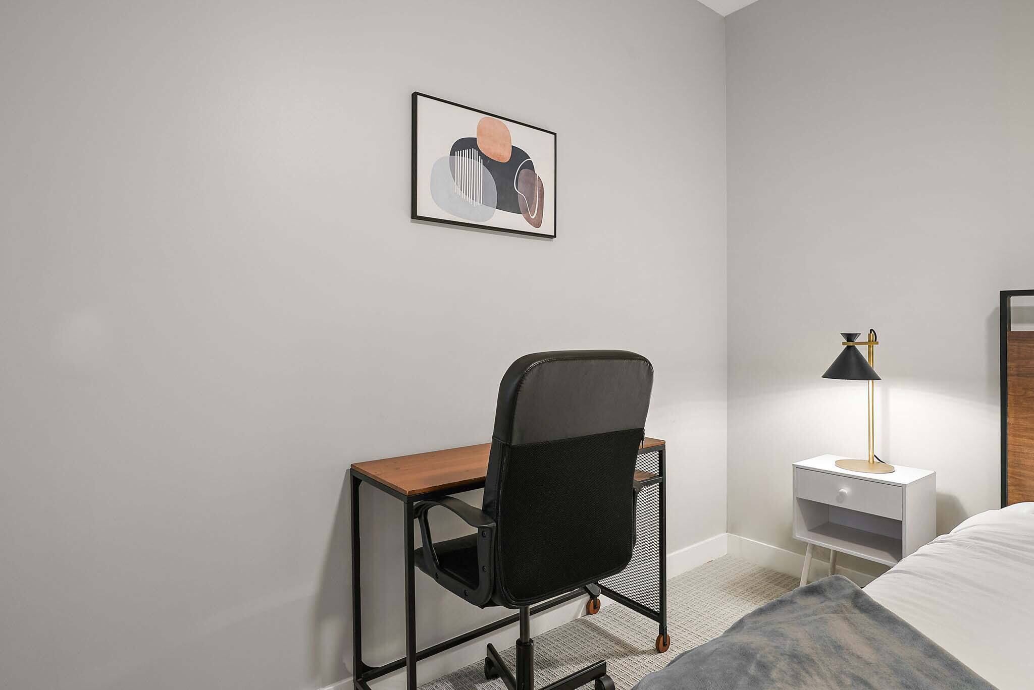 Ett modernt hotellrum med ett skrivbord, en stol, ett sängbord, en lampa och en säng.