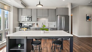 A modern kitchen with a large island, stainless steel appliances, and a view to the outside. - CozySuites Marquee (Minneapolis)