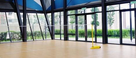 An indoor sports hall with a wooden floor, large windows, and a yellow mop.