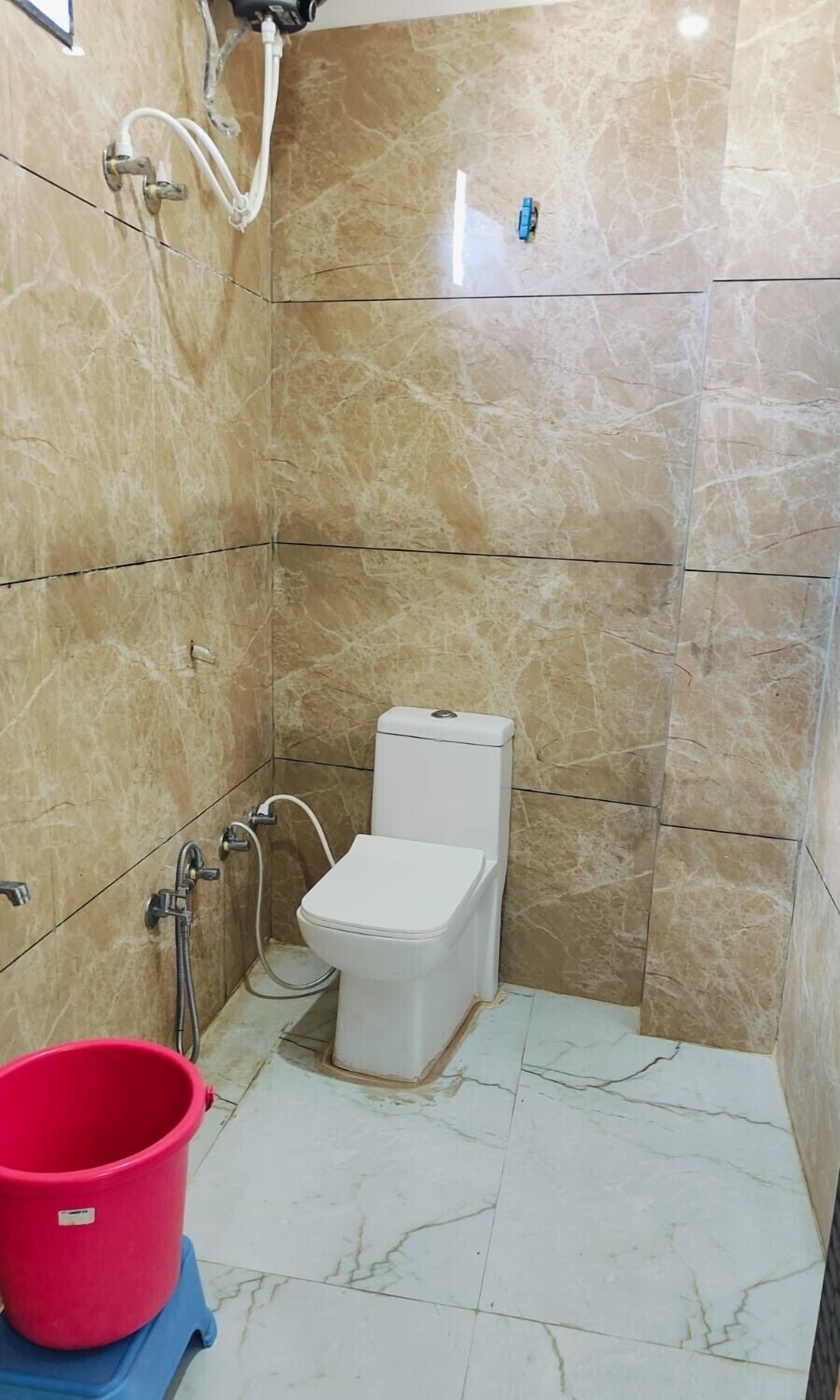 A small, tiled bathroom with a toilet, a shower, and a red bucket.