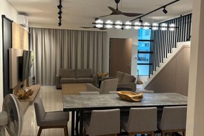 Una sala de estar moderna con un sofá, una mesa de comedor y sillas. Hay un televisor en la pared y un ventilador de techo.