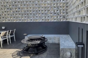 Un área de estar al aire libre moderna con una mesa redonda y sillas, una pared con cajas de almacenamiento y una pared gris.