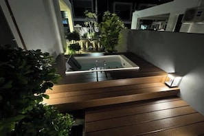 A modern outdoor bathroom with a rectangular tub, wooden steps, and a small illuminated light fixture.