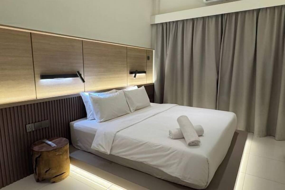 A modern hotel room with a large bed, wooden headboard, and a small wooden stool.