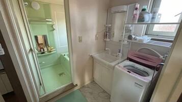 A compact bathroom with a shower, a washing machine, and a small sink.