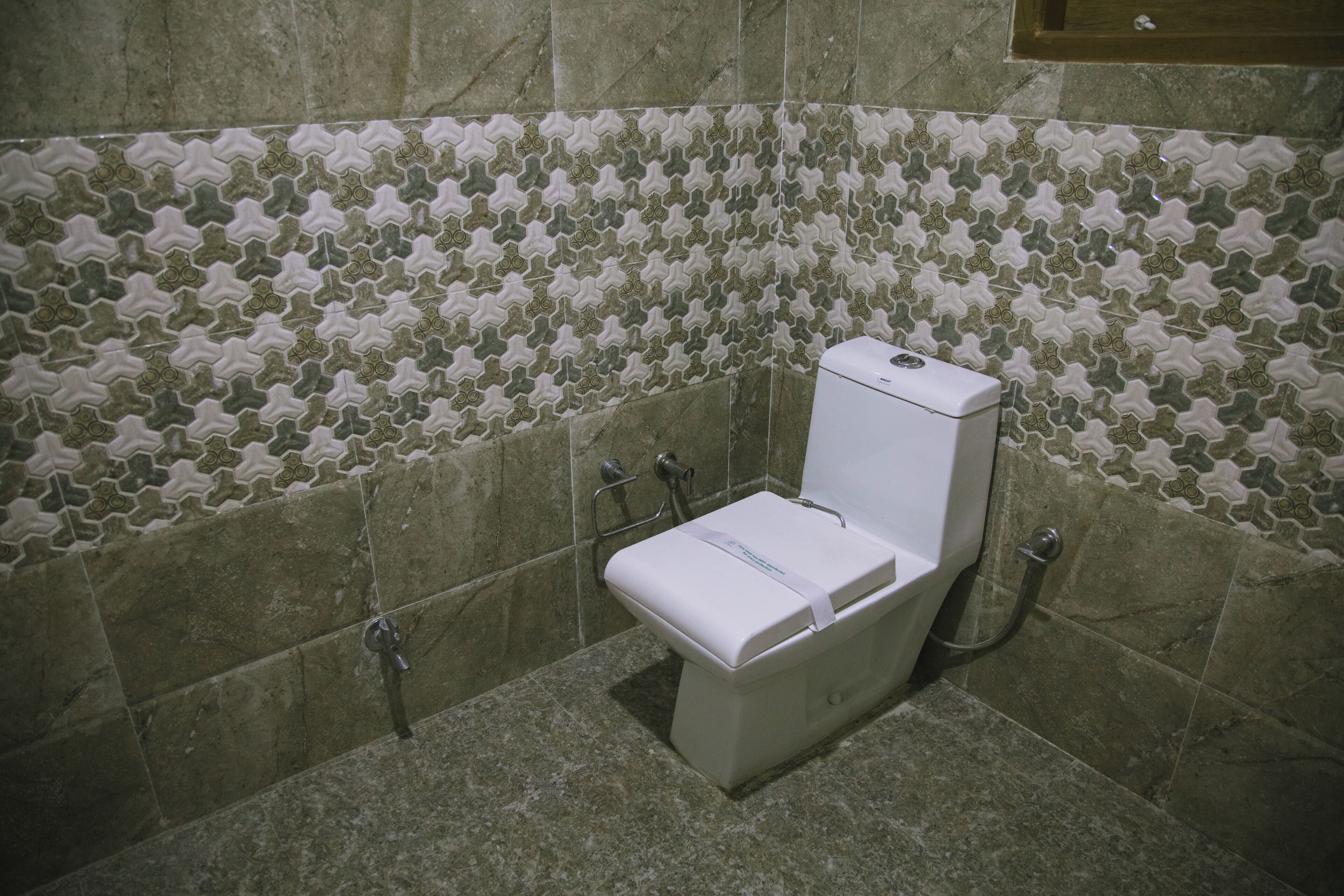 A bathroom with a toilet, a shower, and a tiled wall with a geometric pattern.