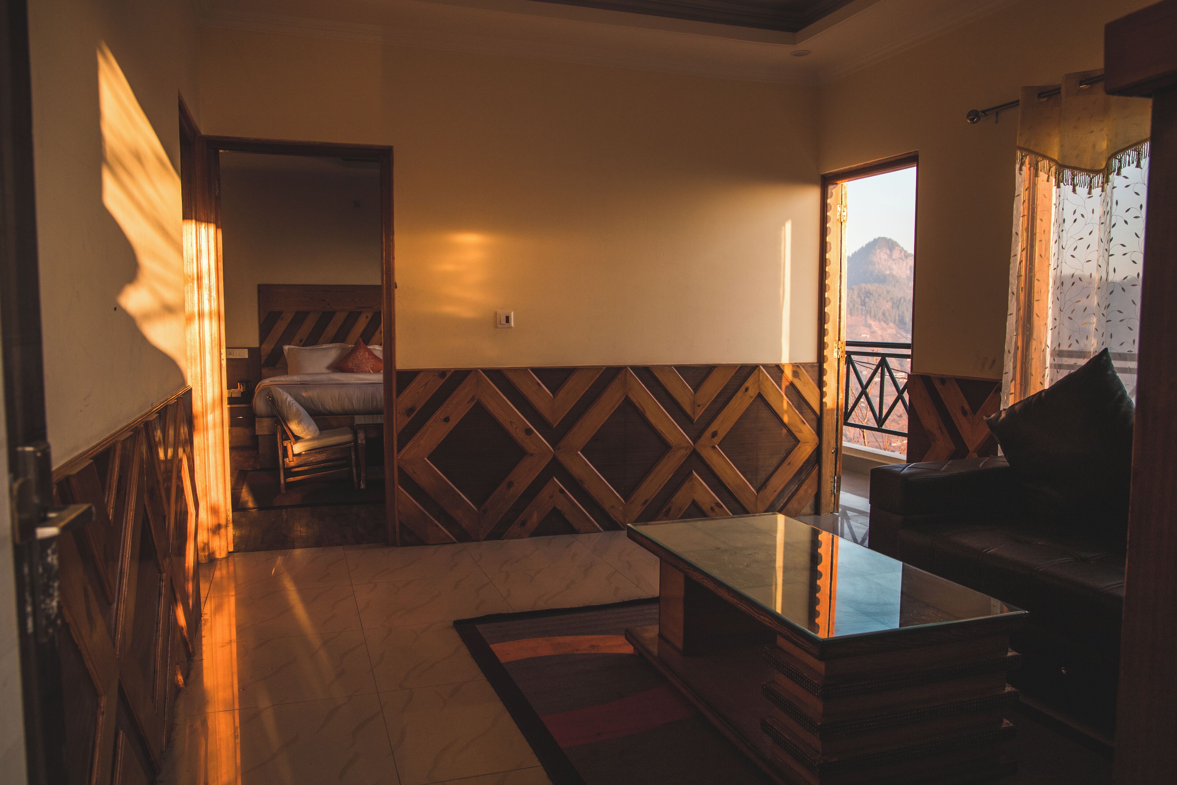 A room with a bed, a sofa, a table, and a view of mountains.