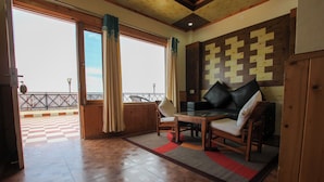 A room with a wooden floor, a checkered outdoor area, a table with chairs, and a view through large windows. - Hilltop Resort, Narkanda (Theog)