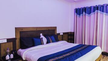 A neatly made bed with a wooden headboard, a bedside table with a bottle and a tissue box, and a window with purple curtains.