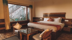 A hotel room with a large bed, a wooden headboard, a glass table, two chairs, and a view of a staircase outside. - Hilltop Resort, Narkanda (Theog)