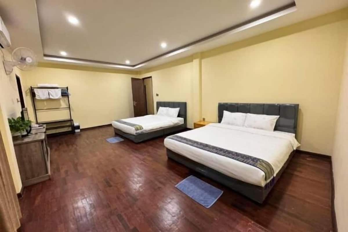 A hotel room with two beds, wooden flooring, a small desk with a plant, and a wardrobe.