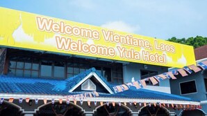 Een gebouw met een groot geel bord waarop staat: 'Welcome Vientiane, Laos Welcome Yula Hotel'.