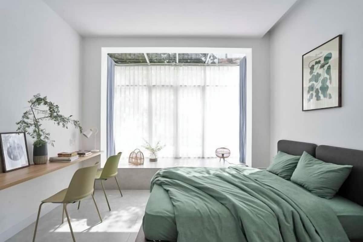A bedroom with a bed, a desk, chairs, a window with curtains, and a framed picture on the wall.