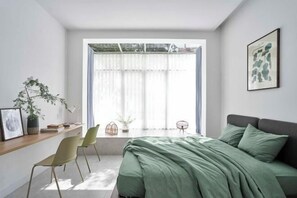 A bedroom with a bed, a desk, chairs, a window with curtains, and a framed picture on the wall. - Express by M Village 47 Thao Dien, a brand of Modern Village Lifestyle (Ho Chi Minh City)