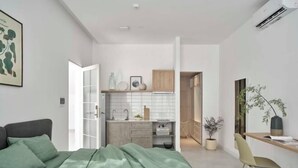 A modern bedroom with a bed, a desk, and a kitchenette.