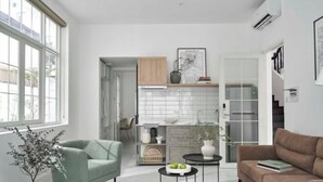A modern living room with a sofa, armchair, and coffee table, a kitchen area with cabinets and a window, and a framed map on the wall.