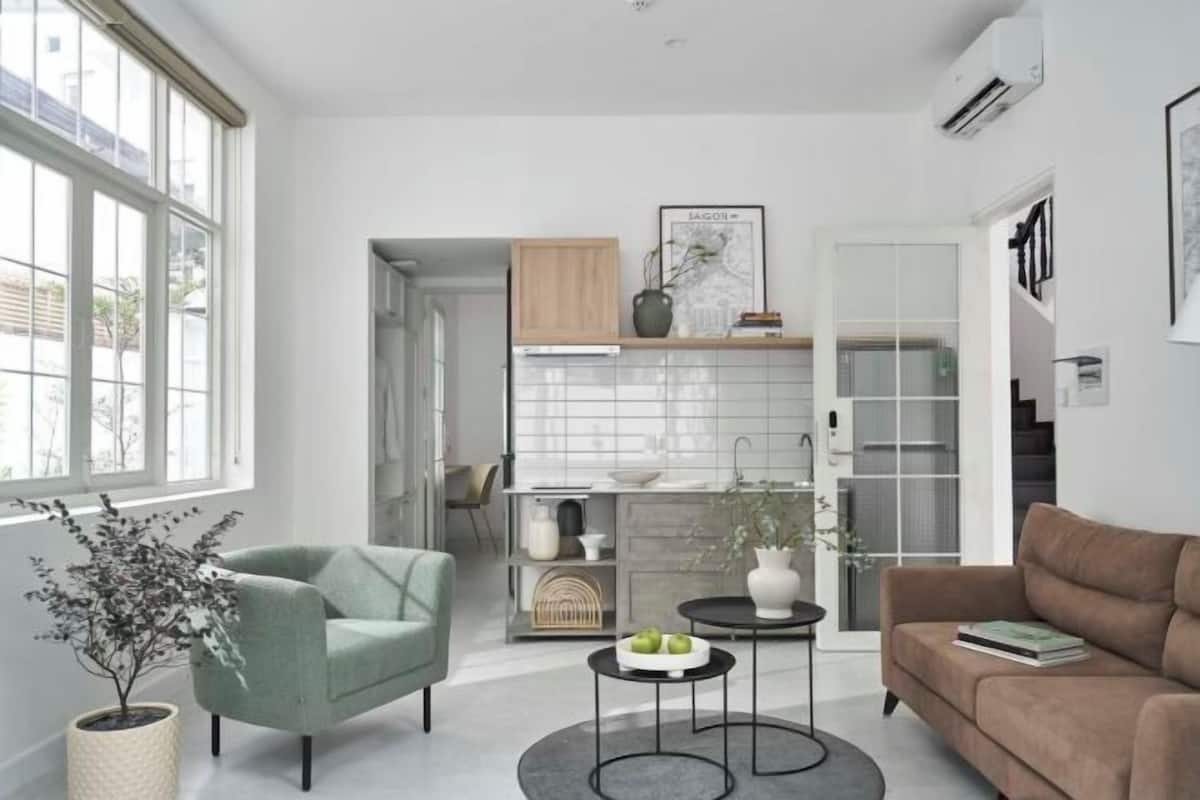A modern living room with a sofa, armchair, and coffee table, a kitchen area with cabinets and a window, and a framed map on the wall.