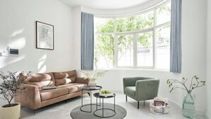 A modern living room with a leather sofa, a green armchair, a round coffee table, and a large window with curtains.
