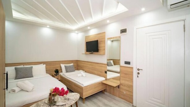 A compact hotel room with two beds, a small table with a vase, a mounted TV, and a white door. - New Life Taksim Hotel (Istanbul)